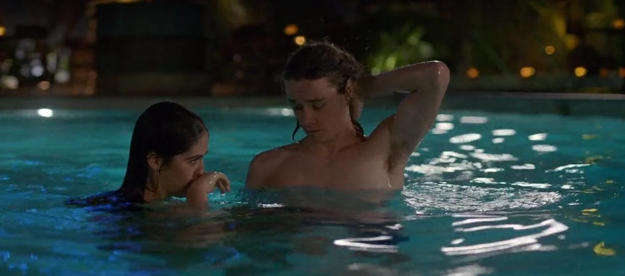 Two people conversing in a swimming pool at night.