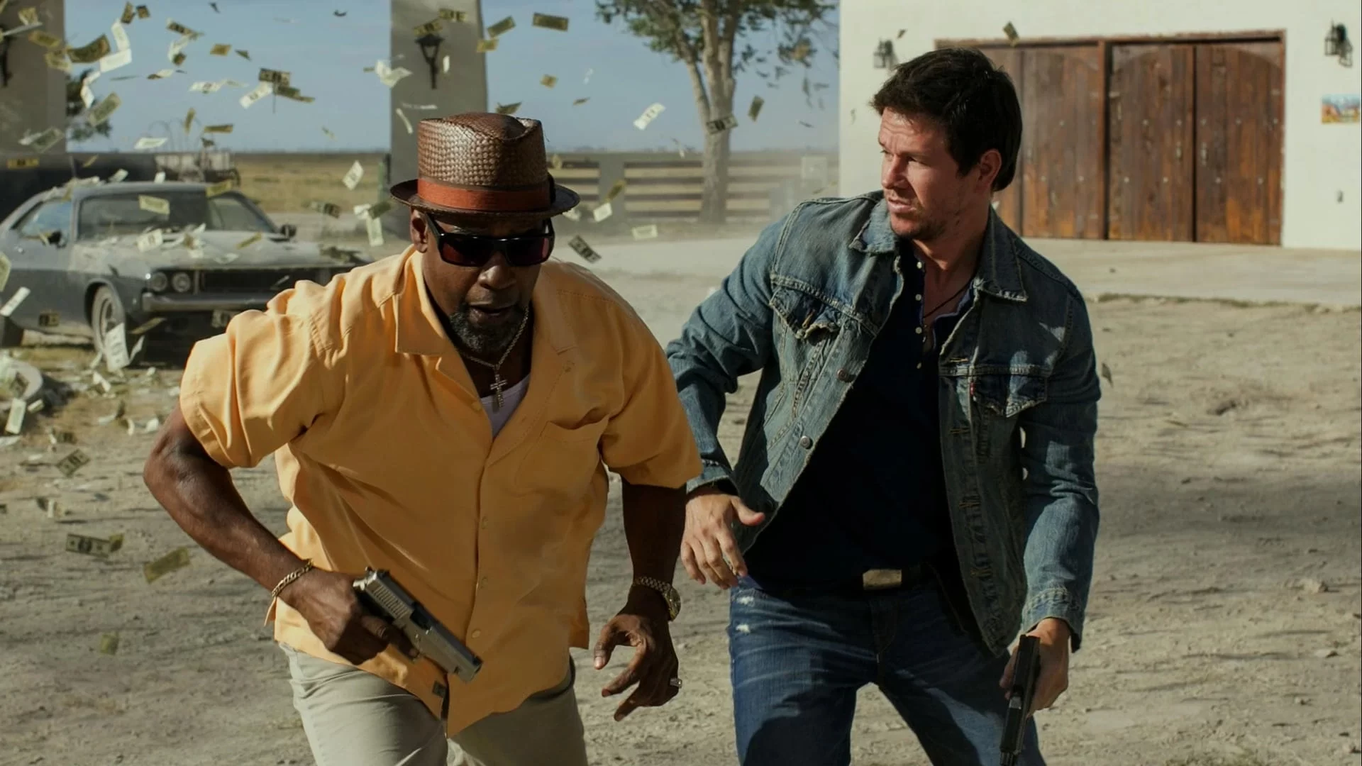 Two men holding guns run in a dusty outdoor setting as money flies around them. A vintage car and buildings are in the background.